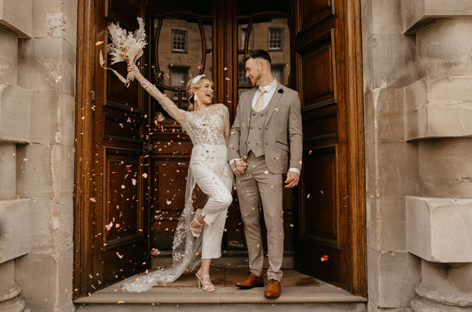 Newly married couple outside Bath's Guildhall. Bride is lifting a floral arrangement and smiling at the groom. There is a sprinkle of confetti.