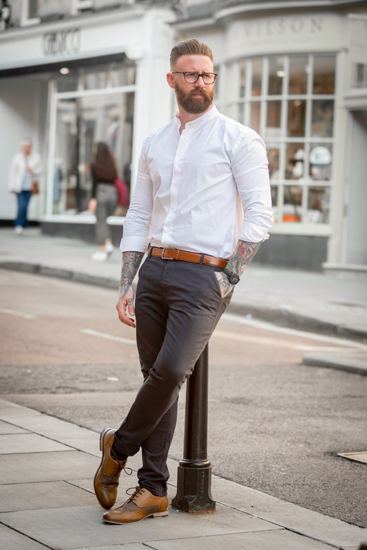 Stylish tattooed gentleman wearing white shirt with sleeves rolled up, chinos and brogue shoes.