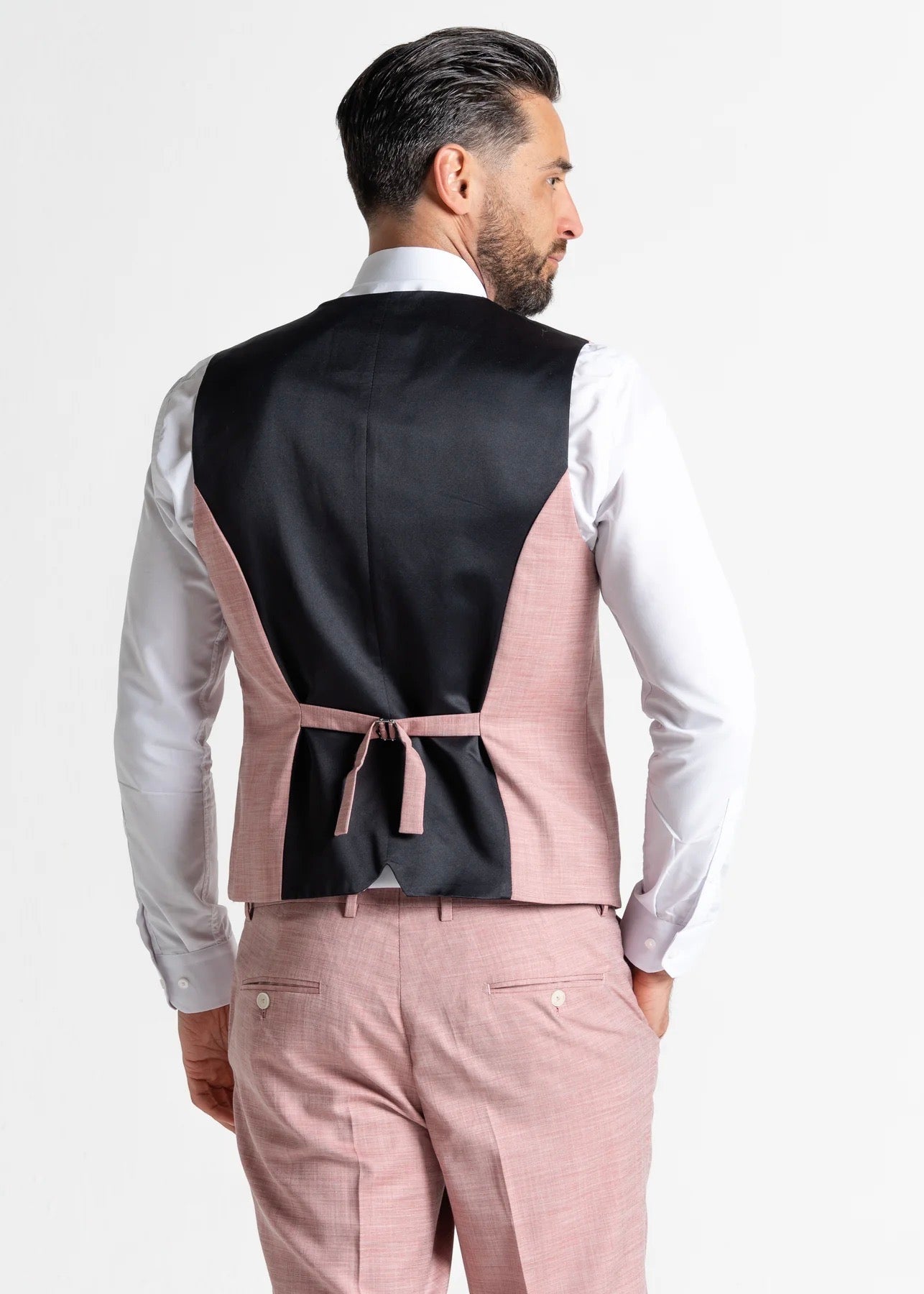 Model wearing the Edward Pastel Pink waistcoat and trousers has his back to the camera, showing the reverse details of the waistcoat and trousers.