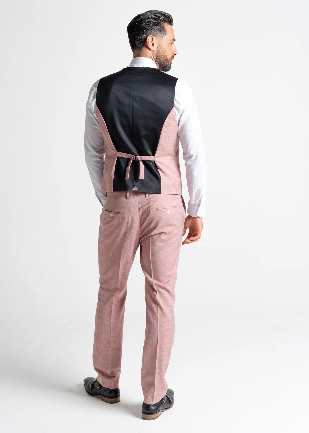 Model wearing the Edward Pastel Pink waistcoat and trousers has his back to the camera, showing reverse details of the pink waistcoat for men. 